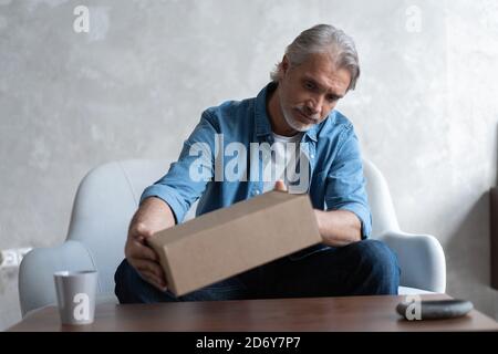 Lächelnder Mann Verbraucher offenen Karton erhalten Postpaket, männliche Kunde erhalten Kartonpaket sitzen auf Sofa zu Hause Stockfoto