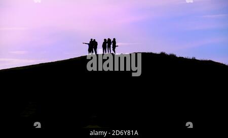 Ein Panoramabild von einer Gruppe von Urlaubern, die auf stehen Der Gipfel des Pentire Point East silhouetted gegen eine bunte Abendlicht in Newquay in Stockfoto