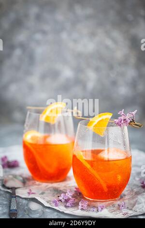 Orange Aperol Spritz Cocktail in einem Weinglas serviert, dekoriert mit einer Scheibe Orange und Flieder Stockfoto