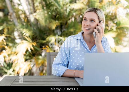 Junge Geschäftsfrau im Gespräch auf dem Smartphone und arbeiten am Laptop im Freien. Glücklich Lächeln. Stockfoto
