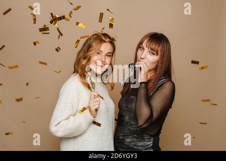 Zwei junge Frauen auf beigem Hintergrund mit goldenem Konfetti haben Spaß und feiern weihnachten. Stockfoto