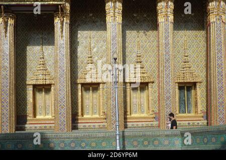 Ein Thailänder, der sein kleines Kind trägt, passiert die verzierte, goldene Viharn (vihan) oder Gebetshalle des Wat Ratchabophit (Rajabophit), Bangkok, Thailand, Stockfoto