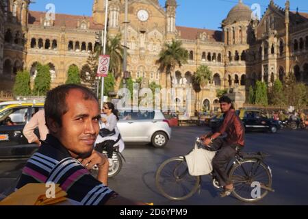 Ein Fußgänger, ein Radfahrer und motorisierter Verkehr vor dem berühmten Chhatrapati Shivaji Maharaj Terminus (CSMT), einem UNESCO-Weltkulturerbe in Mumbai, Indien Stockfoto