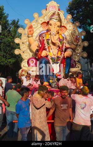 Während Ganesh Chaturthi (Ganesh Festival) wird ein Wagen mit einer Statue des elefantengottes Ganesh von eifrigen Anhängern gezogen, die mit farbigen Pulvern bedeckt sind Stockfoto