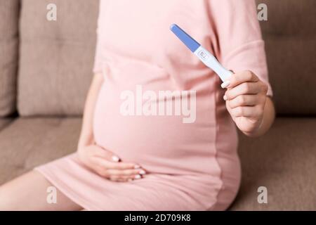 Junge Frau auf dem Sofa sitzen und zeigen Schwangerschaft Testergebnisse. Stockfoto