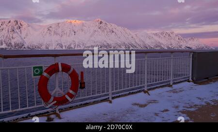 Sørøysundet, Norwegen - 03/02/2019: Rettungsring mit Schiffsname, der an der Reling des Oberdecks des Hurtigruten Kreuzfahrtschiffes mit purpurfarbenem Himmel angebracht ist. Stockfoto