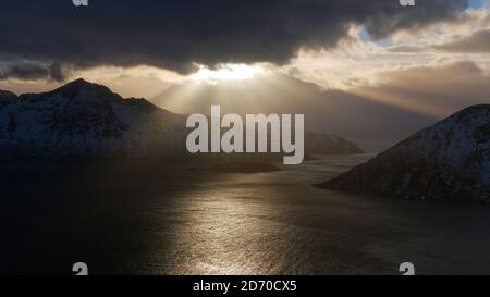 Atemberaubende Luftaufnahme der golden schimmernden Nachmittagssonne, die durch Wolken über den Fjorden bei Rekvik, Troms Og Finnmark, Norwegen scheint. Stockfoto