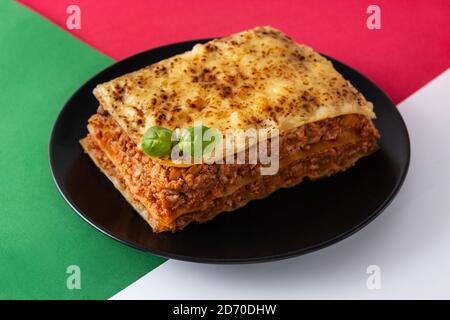 Stück Fleischlasagne auf rotem, weißem und grünem Hintergrund Stockfoto