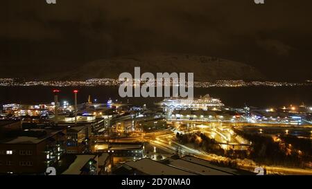 Tromsø, Norwegen - 02/23/2019: Panorama-Luftaufnahme des nördlichen Tromsø bei Nacht mit beleuchteten Straßen und Gebäuden und Aida Kreuzfahrtschiff vor Anker. Stockfoto