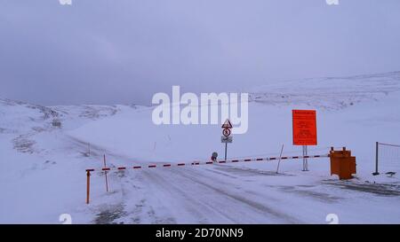 Skarsvåg, Norwegen - 02/28/2019: Geschlossenes Tor an der Straße zum beliebten Nordkapp (Nordkap) im Winter mit orangefarbenem Schild, das über die Konvoi-Stunden informiert. Stockfoto