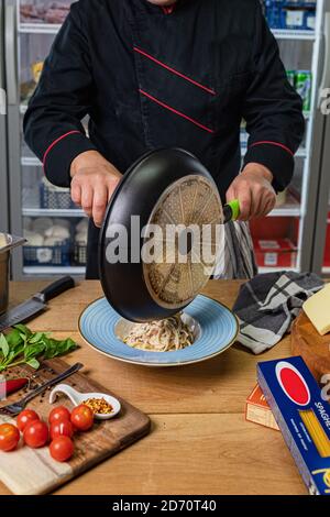 Der Koch legt Pasta aus der Pfanne und die Beschichtung. Stockfoto