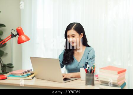 Engagierte Freiberuflerin in Brille und kabellosen Kopfhörern lächelnd Kamera beim Sitzen auf Laptop mit Tasse Stockfoto