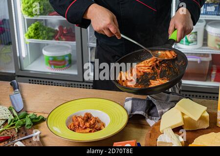 Der Koch legt Pasta aus der Pfanne und die Beschichtung. Stockfoto