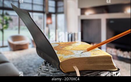 Buch Bibel mit Bleistift öffnen, auf dem Hintergrund des Wohnzimmers. Lesen eines Buches in einer gemütlichen Umgebung. Nahaufnahme. Stockfoto