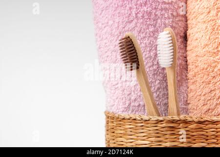 Bambuszahnbürsten mit Handtüchern in einem Korbkorb aus Holz mit Kopierplatz auf weißem Hintergrund. Spa, gesunde Lebensweise und Ökologie Konzept. Stockfoto