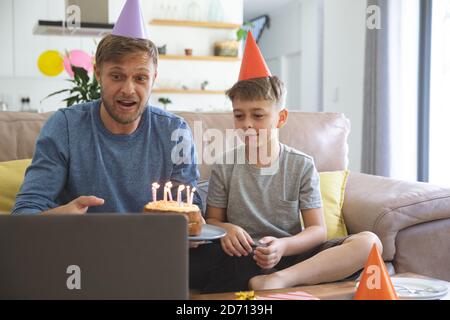 Kaukasischer Mann verbringt Zeit zu Hause mit seinem Sohn zusammen, mit Geburtstagsfeier mit Laptop-Computer für Video-Chat. Soziale Distanzierung während Covid Stockfoto