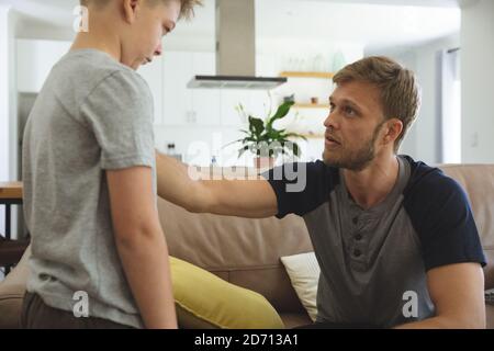 Kaukasischer Mann zu Hause mit seinem Sohn zusammen, sitzt auf dem Sofa im Wohnzimmer, Vater Blick auf traurigen Jungen. Soziale Distanzierung während des Covid 19 Coronavirus Stockfoto