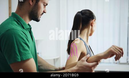 Arzt hilft Frau durch Schulterbehandlung mit Kinesio-Band Stockfoto