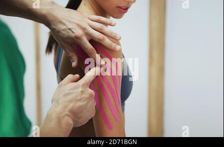 Arzt hilft Frau durch Schulterbehandlung mit Kinesio-Band Stockfoto