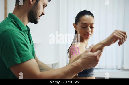 Arzt hilft Frau durch Schulterbehandlung mit Kinesio-Band Stockfoto