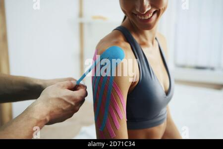 Arzt hilft Frau durch Schulterbehandlung mit Kinesio-Band Stockfoto