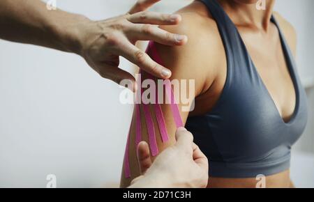 Arzt hilft Frau durch Schulterbehandlung mit Kinesio-Band Stockfoto