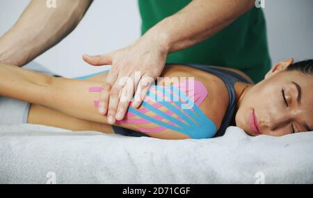 Arzt hilft Frau durch Schulterbehandlung mit Kinesio-Band Stockfoto