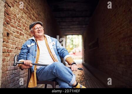 Stylish Senior in modischer Kleidung und in Brille sitzt auf Der Stuhl in der Stadt Stockfoto