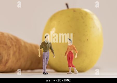 Miniatur Frau und Mann Figur steht neben großen Apfel und Pastinak. Geringe Schärfentiefe des Hintergrunds. Gesundheit, gesunde Lebensweise und Schlankheitskur Stockfoto