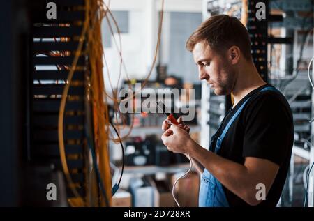 Junger Mann in Uniform mit Messgerät arbeitet mit Internet Ausrüstung und Kabel im Serverraum Stockfoto