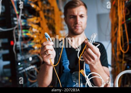 Junger Mann in Uniform fühlt sich verwirrt und auf der Suche nach einem Lösung mit Internet-Ausrüstung und Drähten im Serverraum Stockfoto