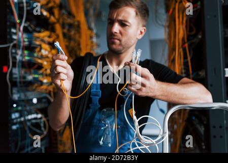 Junger Mann in Uniform fühlt sich verwirrt und auf der Suche nach einem Lösung mit Internet-Ausrüstung und Drähten im Serverraum Stockfoto