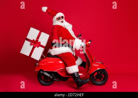 In voller Länge Profil Foto von im Ruhestand Opa weißen Bart reiten Vintage Motorrad High-Speed spät liefern Geschenk tragen weihnachtsmann Kostüm Mantel Sonnenglas Stockfoto