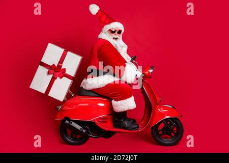 In voller Länge Profil Foto von im Ruhestand Opa weißen Bart reiten Vintage Motorrad liefern Geschenk heiligabend tragen weihnachtsmann Weihnachten Kostüm Schutzbrillen Stockfoto