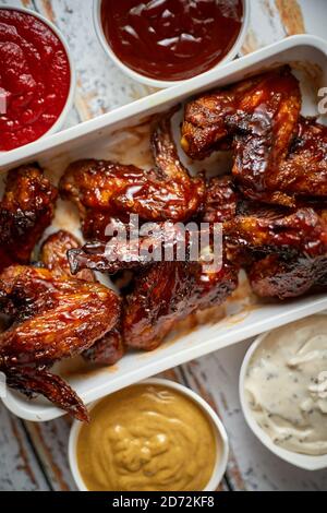 Hähnchenflügel in dicker Grillsauce mit verschiedenen Seiteneinbrüchen. Serviert auf einer weißen gusseisernen Schüssel Stockfoto