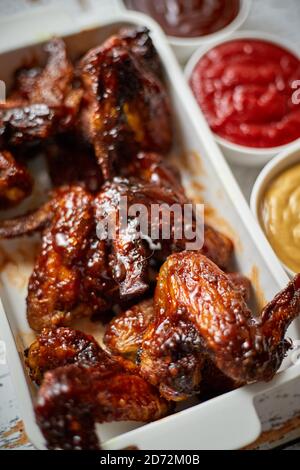 Hähnchenflügel in dicker Grillsauce mit verschiedenen Seiteneinbrüchen. Serviert auf einer weißen gusseisernen Schüssel Stockfoto