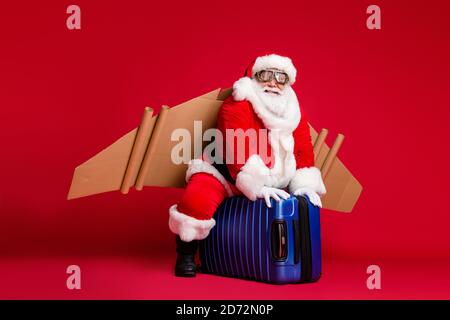 In voller Länge Foto von im Ruhestand kindisch Opa weißen Bart reiten Koffer reaktiv Jetpack Pilot aufsteigend Himmel tragen weihnachtsmann Kostüm Brillen Stockfoto