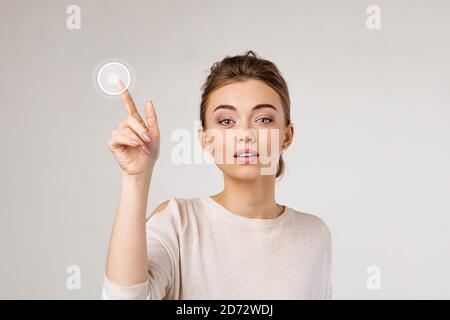 Junge schöne Frau drücken virtuelle Taste und Blick auf die Kamera auf grauem Hintergrund. Stockfoto