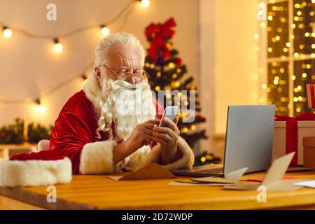 Moderne Santa mit mobilen E-Mails von Kindern lesen und Bestellung zeigt Lieferung an Stockfoto