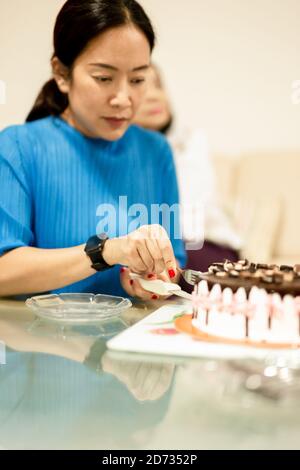 Frauenhände schneiden Geburtstagskuchen auf dem Tisch. Stockfoto