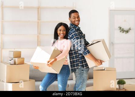 Fröhliche schwarze Paar Umzug in neue Residenz zusammen, hält Habseligkeiten am Umzugstag Stockfoto