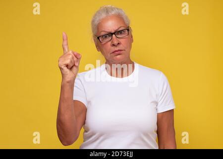 Frau mittleren Alters trägt in einer Brille zeigt mit dem Finger nach oben Mit ernsthafteren Worten Stockfoto