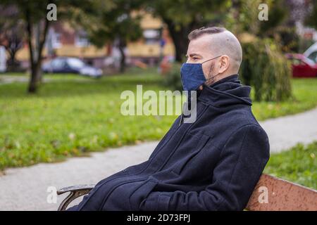 Ein Mann sitzt auf einer kaputten Bank im Tropfender Regen im Park Stockfoto
