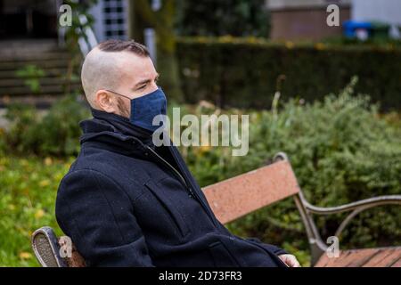 Ein Mann sitzt auf einer kaputten Bank im Tropfender Regen im Park Stockfoto