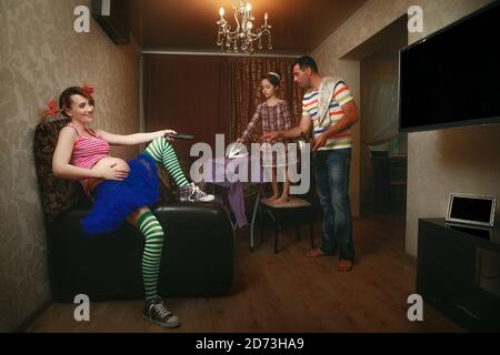 Schwangere Frau schaut fern, während ihr Mann und ihre Tochter Bügeln Sie ein Hemd im Wohnzimmer Stockfoto