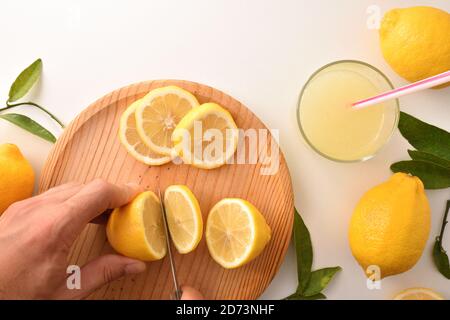 Hände schneiden eine Zitrone, um eine Limonade auf der Küchenbank vorzubereiten. Draufsicht. Horizontale Zusammensetzung. Stockfoto