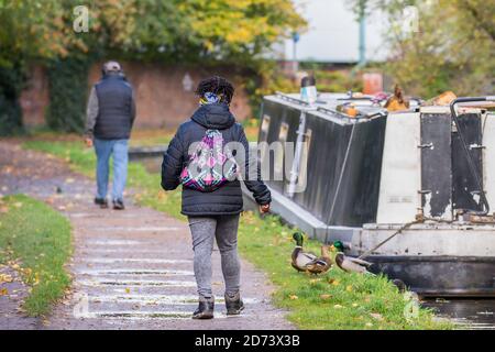 Rückansicht von Fußgängern, die entlang des britischen Kanals towpath, vorbei an einem festfahrenden Schmalboot, Kanalboot, im Herbst gehen. Stockfoto