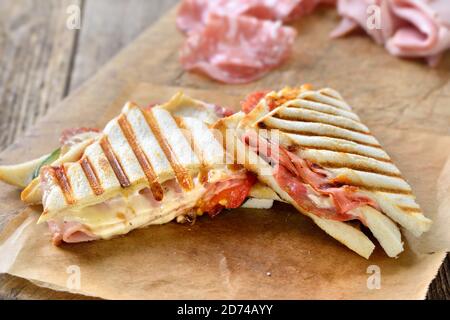 Gepresste Doppelpanini mit italienischer Salami, Schinken und Käse frisch vom Kontaktgrill auf Sandwichpapier serviert Stockfoto