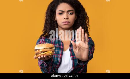 Schwarze Frau Hält Burger Und Zeigt Stop-Geste Stockfoto