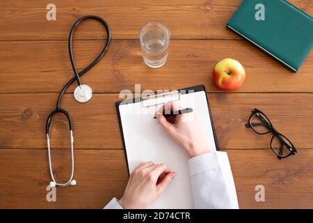 Empfehlungen und Rezept von Arzt. Frau im weißen Mantel schreibt auf Tablette am Arbeitsplatz Stockfoto